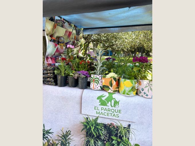 El puesto de El Parque Macetas en la feria, con jardines colgados a un costado y macetas sublimadas con plantas sobre la mesa