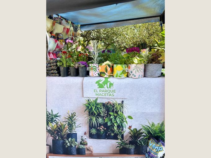 El puesto de El Parque Macetas en la feria, con sublimadas y plantas en el estante de arriba y un jardín vertical en el frente