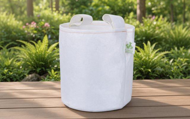 Maceta geotextil blanca con asas, apoyada sobre una tarima de madera en el jardín