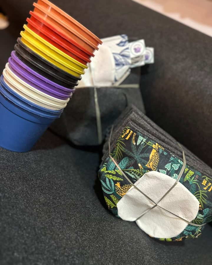 Pila de macetas recicladas de colores junto a macetas de tela y sublimadas plegadas